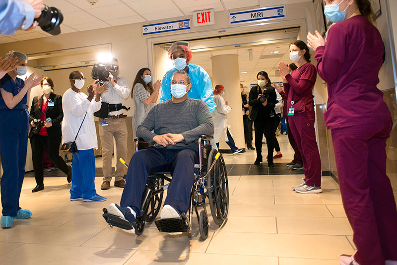 A recovered COVID-19 patient meets applause and camera flashes on their way out of the hospital.